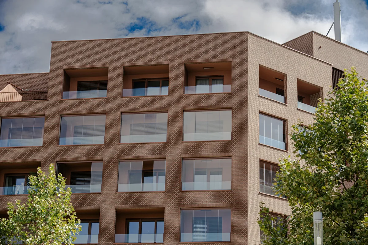 Un edificio de viviendas moderno de ladrillo con balcones acristalados y árboles delante